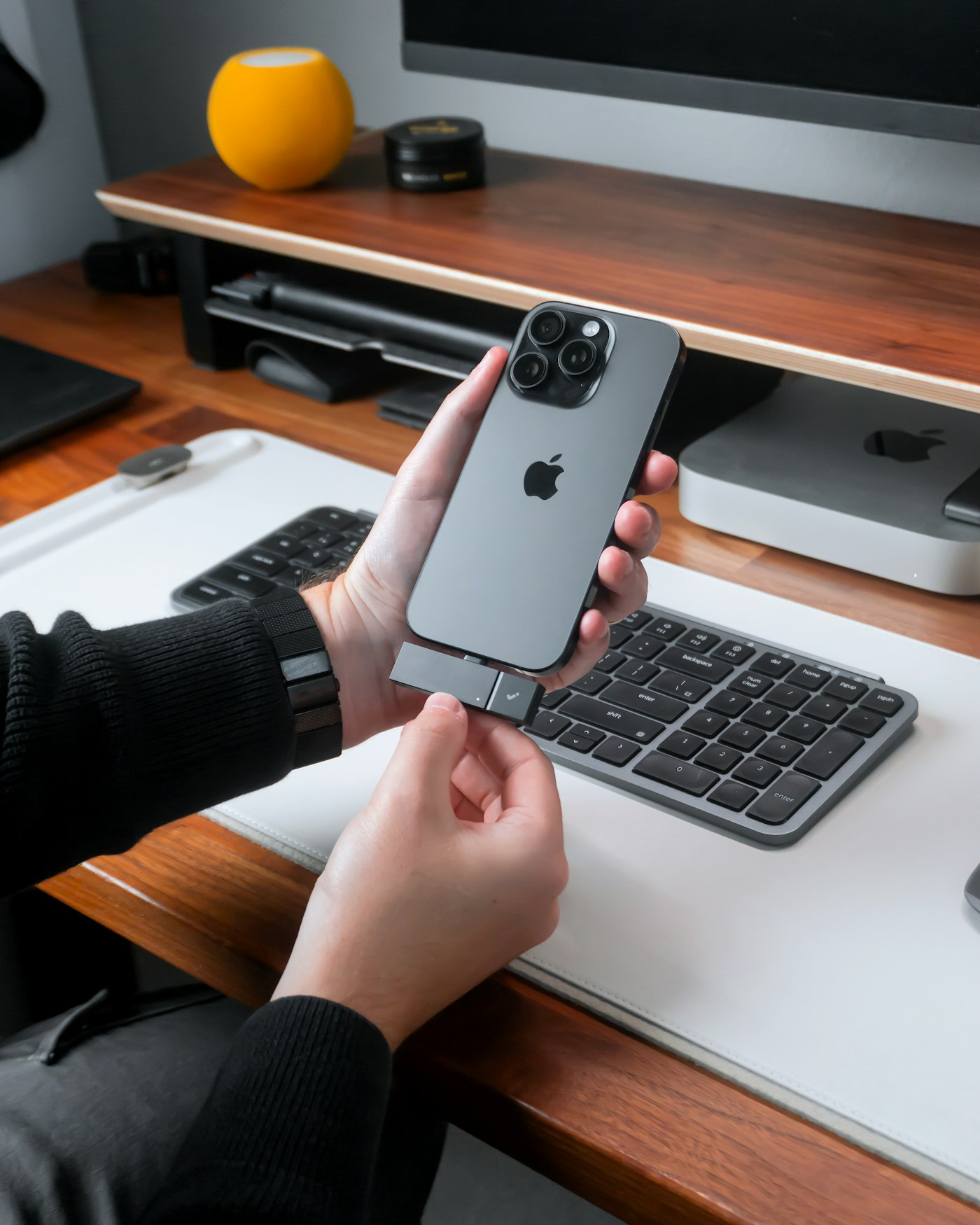 A hand holding an iPhone in a calm workspace.